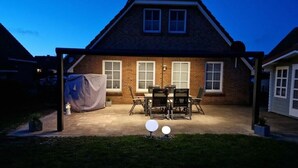 Ein Backsteinhaus mit überdachter Terrasse, einem Tisch und Stühlen sowie einem Rasen.