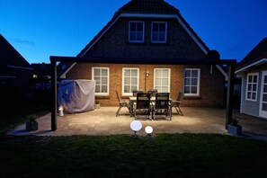 Ein Backsteinhaus mit überdachter Terrasse, einem Tisch und Stühlen sowie einem Rasen.
