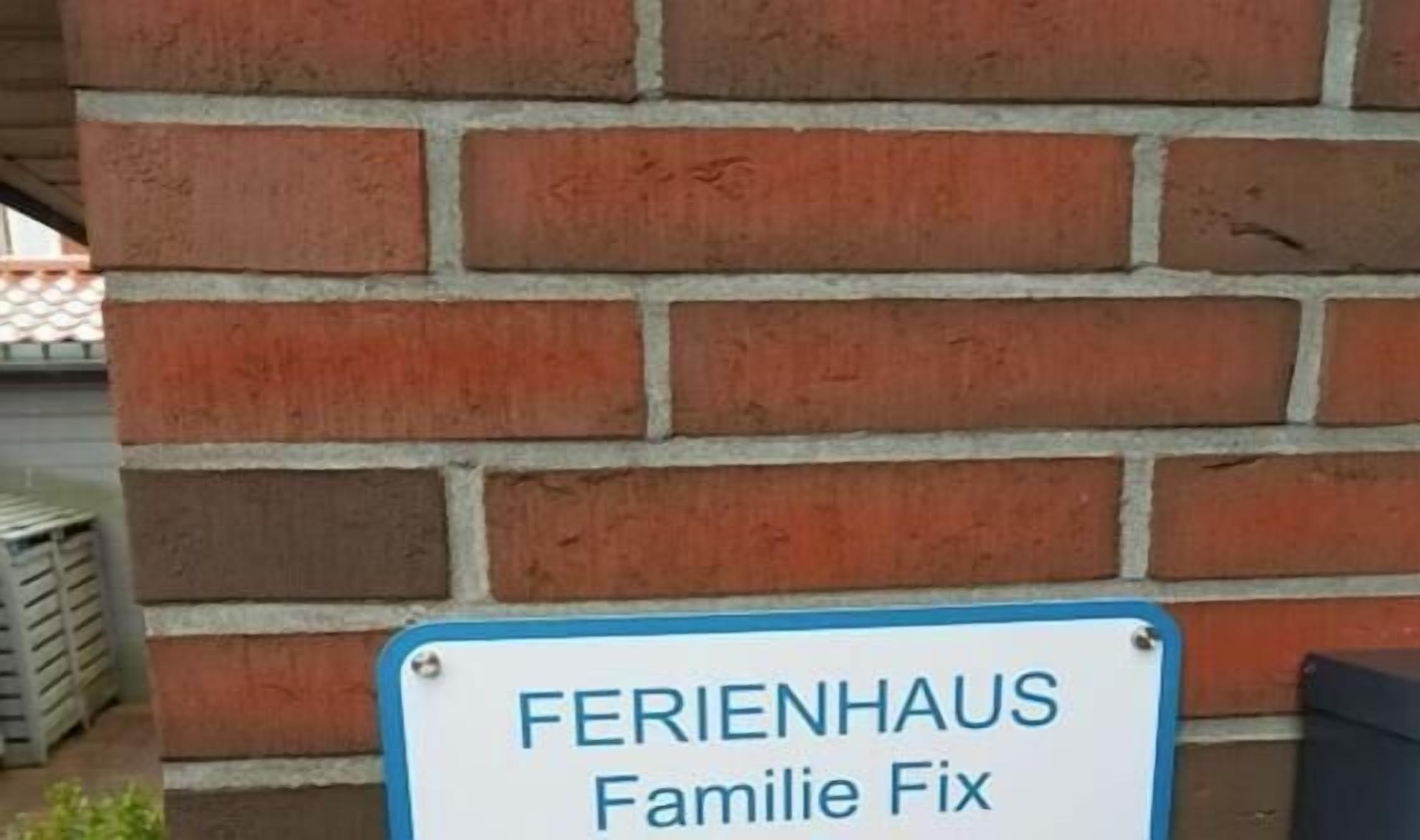 Un cartel con el texto 'FERIENHAUS Familie Fix' frente a una pared de ladrillo.