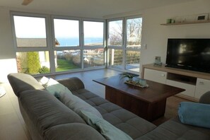 A modern living room with a large window, a flat-screen TV, and a sofa. - Baltic Sea harbor view (Langballig)