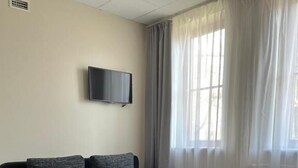 Habitación de hotel con cama, sofá, televisor de pantalla plana y ventanas amplias con cortinas.