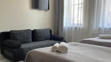 A hotel room with a bed, a sofa, a flat-screen TV, and large windows with curtains.