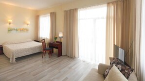 A hotel room with a bed, desk, chair, TV, and curtains.