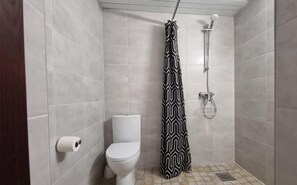 Un baño pequeño con azulejos, un inodoro, una cortina de ducha y un cabezal de ducha.