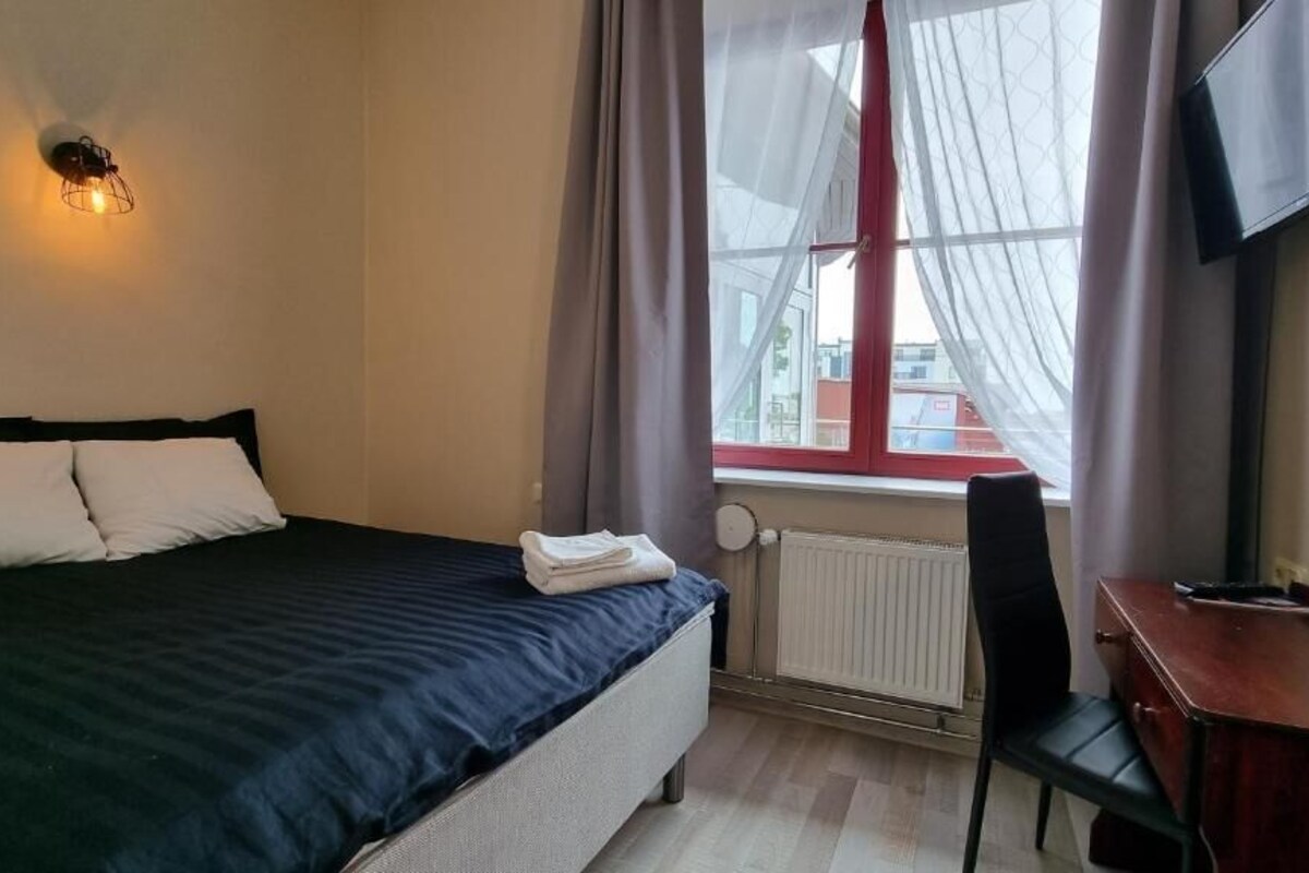 Habitación de hotel con cama, escritorio, silla, radiador y televisor montado en la pared.