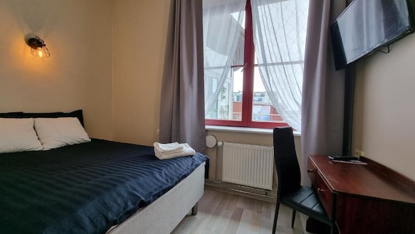 A hotel room with a bed, a desk, a chair, a radiator, and a TV mounted on the wall.