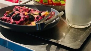 Un bufé de desayuno con diversos platos, un vaso de leche y un recipiente azul con cubiertos.