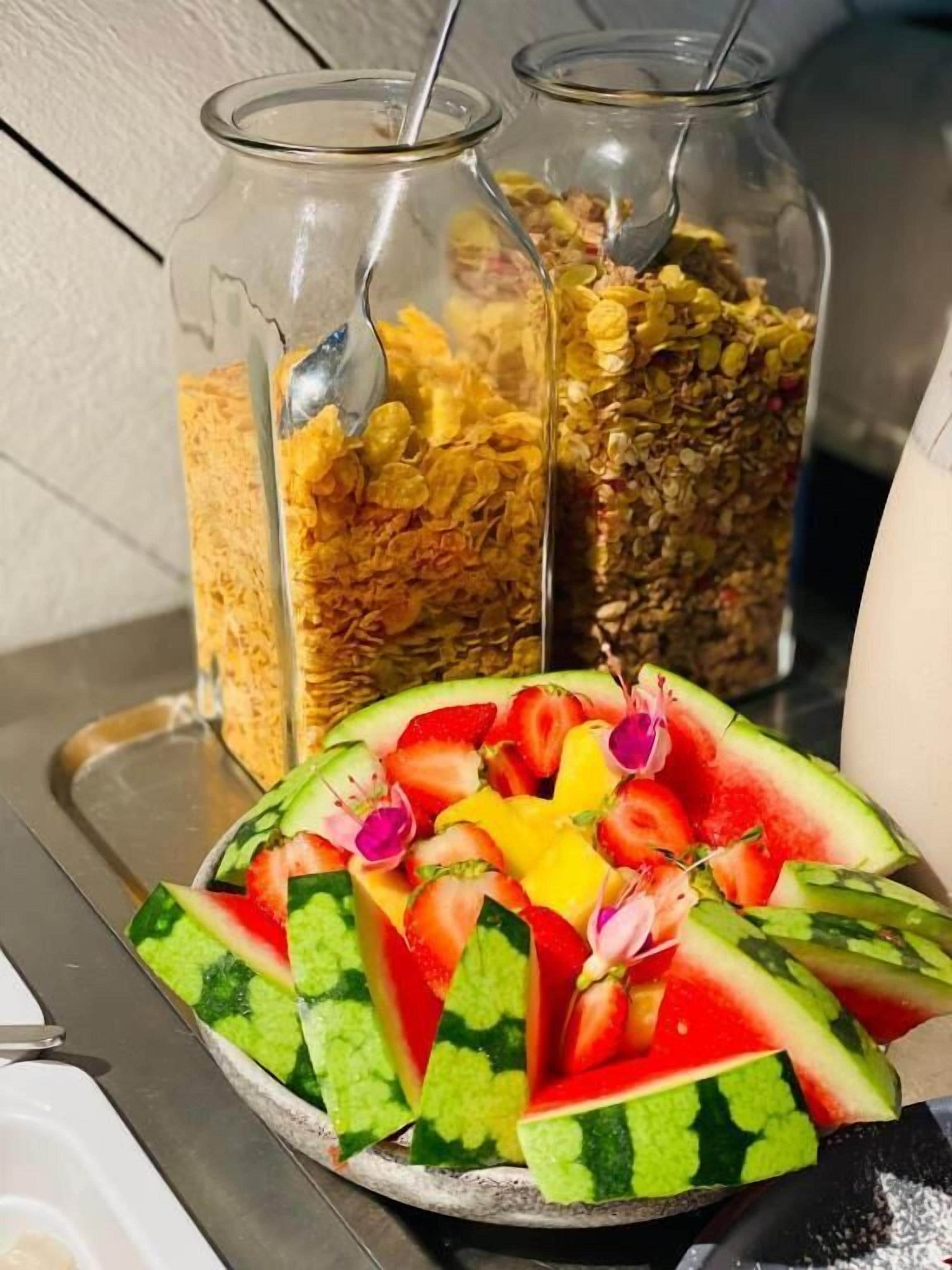 Bandeja de café da manhã com melancia fatiada e diversos cereais em potes de vidro.