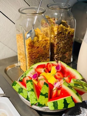 A breakfast tray with sliced watermelon and a variety of cereal flakes in glass jars.