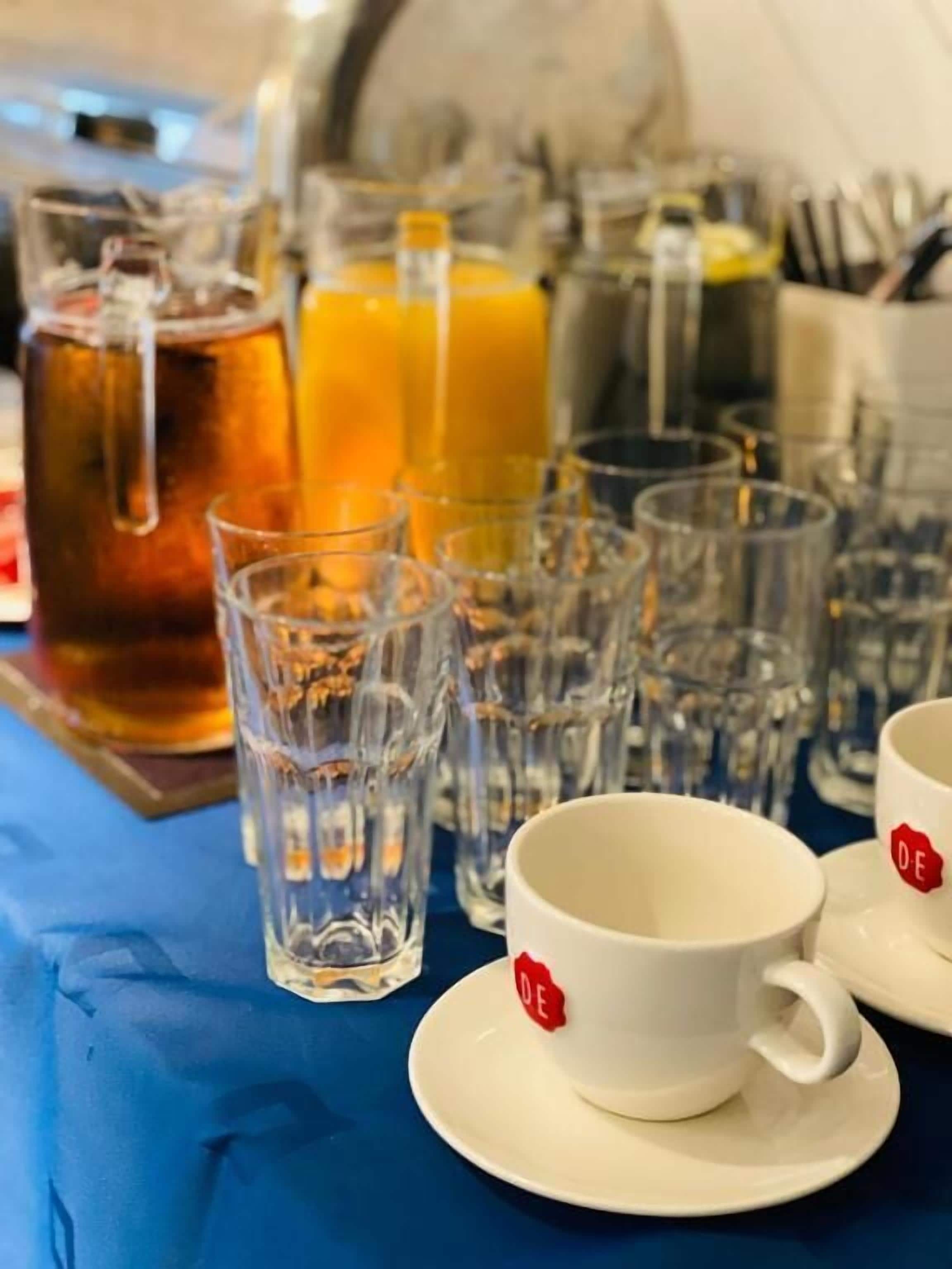 A table with various drink containers and glasses, including a pitcher and bottles, on a blue tablecloth.