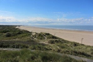 Een strand met heldere lucht, zandstrand en grasduinen.