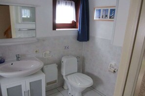 Een compacte badkamer met een wit wastafelmeubel, toilet en spiegel.