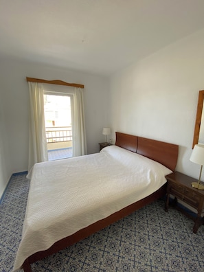Ein Hotelzimmer mit einem Einzelbett, einem Nachttisch mit Lampe, einem Fenster mit Vorhängen und einem gemusterten Boden.