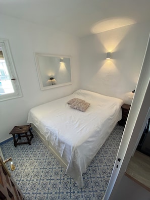 Ein Schlafzimmer mit einem Einzelbett, einem kleinen Hocker, einem Spiegel und einem gemusterten Boden.