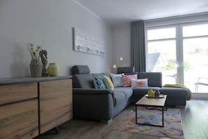 A modern living room with a grey sofa, a wooden sideboard, and a large window with curtains. - "Baltic Sea Love" Villa Lena Wilhelmstrasse (Sellin)