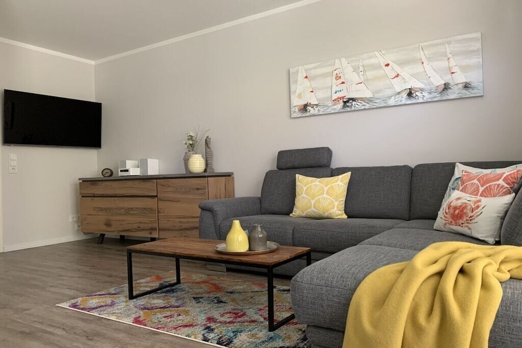 A living room with a gray sofa, a coffee table, a colorful rug, a wooden cabinet, and a painting of sailboats.