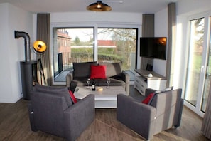 A modern living room with a sofa set, a coffee table, a fireplace, and a television. - Holiday apartment with 2 bedrooms (Fedderwardersiel-Butjadingen)