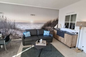 Un salón con vista al mar, un sofá con almohadas que dicen 'HOME', una mesa de centro y un armario de madera.