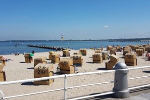 Een strand met genummerde ligbedden en een pier op de achtergrond.