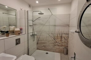 Een moderne badkamer met een douchecabine van glas, een witte wastafel en een grote spiegel.