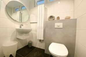 Ein Badezimmer mit rundem Spiegel, Waschbecken, Toilette und Handtuchhalter.