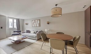 Ein modernes Wohnzimmer mit einer Couch, einem Esstisch mit Stühlen, einem Couchtisch, einer Lampe und einer Pendelleuchte.