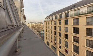 Ein mehrstöckiges Gebäude mit Balkonen, im Hintergrund ein Fluss und ein klarer Himmel.