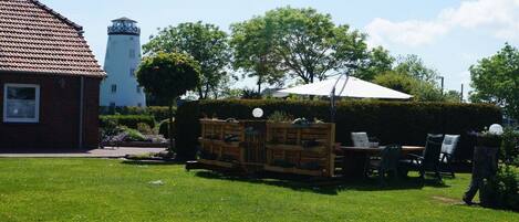 A garden with a wooden bench, a table, and chairs, a white umbrella, and a hedge.