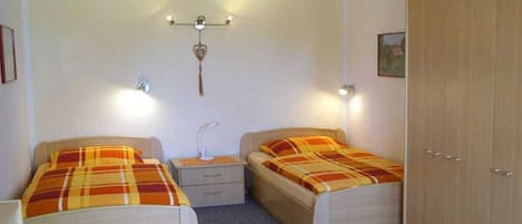 Un dormitorio con dos camas individuales, una mesita de noche, un armario y un aplique de pared.