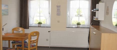 Ein Zimmer mit Holztisch und -stühlen, einem Heizkörper und einem fenster mit Vorhängen.