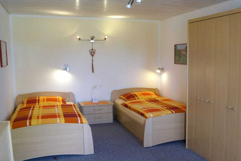 A bedroom with two single beds, a nightstand, a wardrobe, and a wall-mounted light fixture.