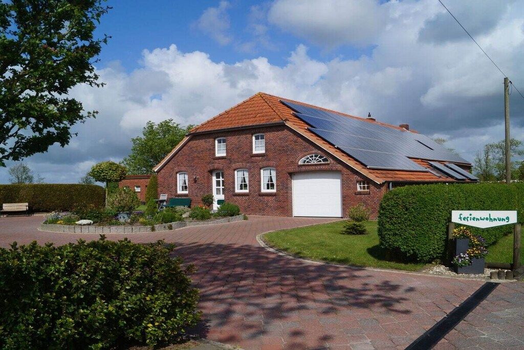 A brick house with a solar panel roof, a driveway, and a well-maintained garden.