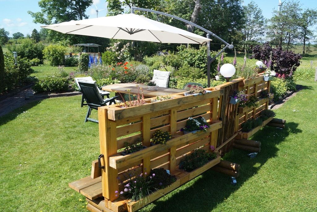 A wooden deck with a table and chairs, surrounded by lush greenery and a large umbrella.