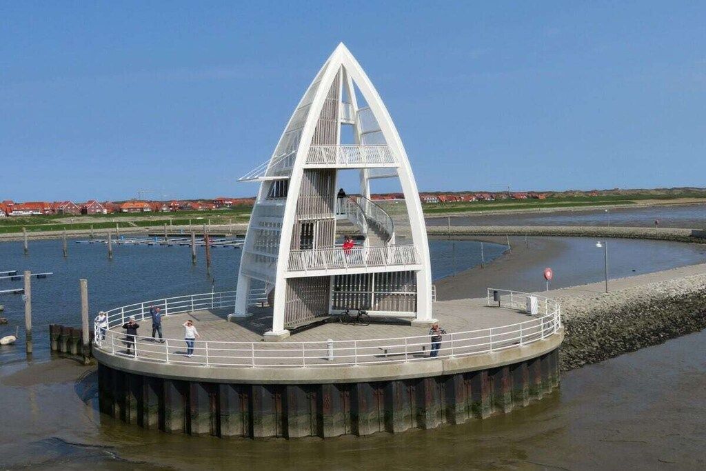 A white, triangular-shaped structure with a spiral staircase, situated on a concrete platform surrounded by water.