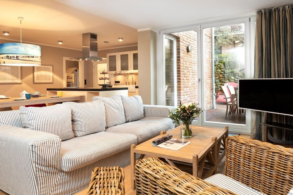 A modern living room with a striped sofa, a wooden coffee table, wicker furniture, and a television.