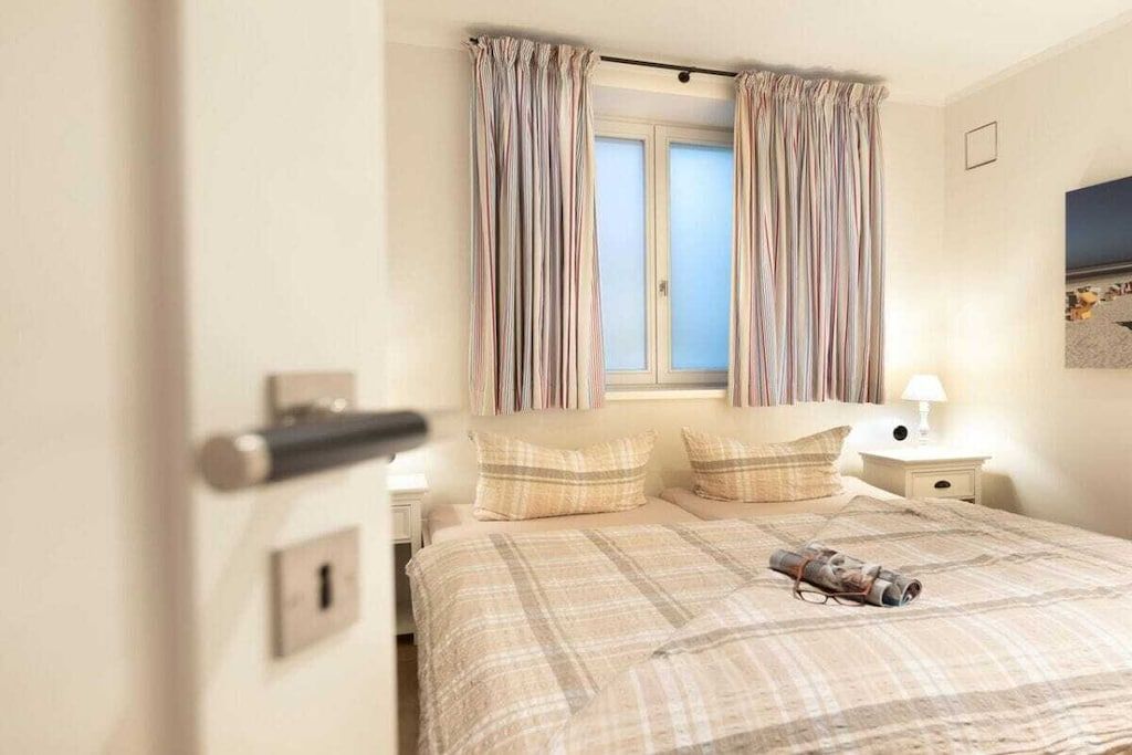 A bedroom with a bed, curtains, a nightstand, and a lamp.