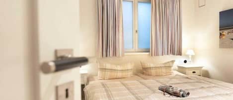 A bedroom with a bed, curtains, a nightstand, and a lamp.