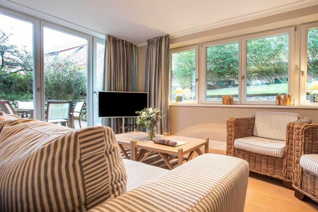 Ein Wohnzimmer mit einer Couch, einem Fernseher, einem Tisch mit einer Vase und Korbstühlen.