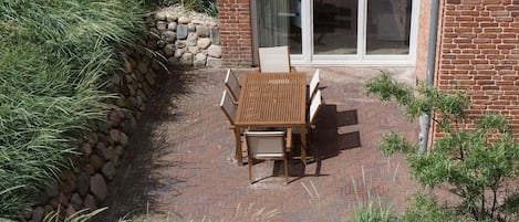 A patio with a table and chairs, a stone retaining wall, and a building with a brick facade and large glass sliding doors.
