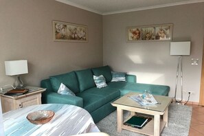 A living room with a green sofa, a glass coffee table, a lamp, and artwork on the walls. - Holiday apartment Meeresbrise (Ostseebad Nienhagen)