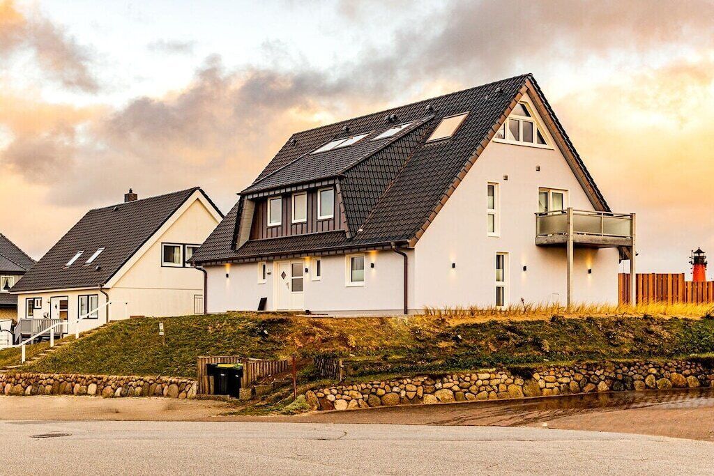 Une rangée de maisons modernes avec des toits en pente, un mur de soutènement en pierre et un ciel dégagé.