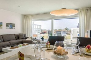 Ein modernes Wohnzimmer mit einer Couch, einem Esstisch und großen Fenstern mit Blick ins Freie.
