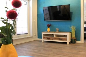 Ein Zimmer mit einem flachbildfernseher an einer türkisfarbenen Wand, einem Holztischchen mit Dekoration und einem Fenster mit Blick.