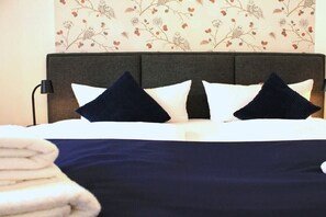 Ein Bett mit dunkelbrauner Kopfteil, weißer Bettwäsche und zwei dunklen Kissen.