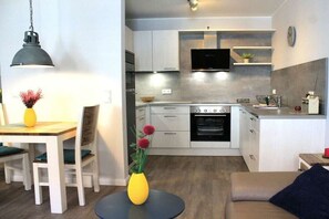 Eine kompakte Küche mit modernen Geräten, ein Essbereich mit Tisch und Stühlen sowie ein Wohnbereich mit einer Couch.