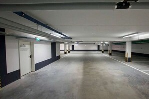 Un parking avec des planchers en béton, des murs blancs et des piliers ornés de rayures jaunes et noires.