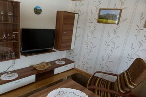 A living room with a flat-screen TV, wooden furniture, a patterned wallpaper, and a framed picture on the wall. - Mehnert's holiday apartment (Reinhardtsdorf)