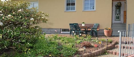 A yellow building with a tiled roof, a front door with a decorative arch, and a small garden area with a table and chairs.