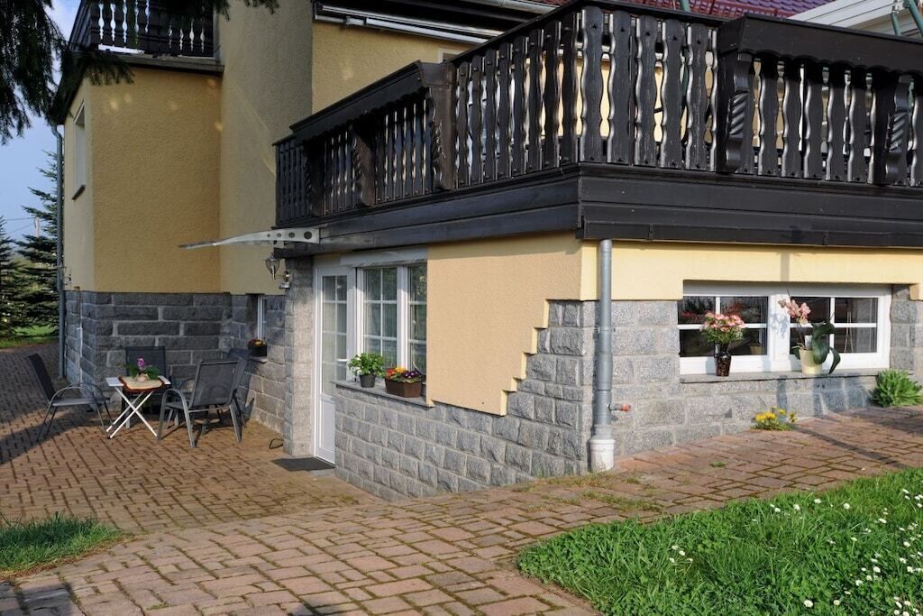 Ein Haus mit einer Stein-Fassade, einem Balkon mit schwarzem Geländer und einer kleinen Sitzgelegenheit im Freien mit Stühlen und einem Tisch.