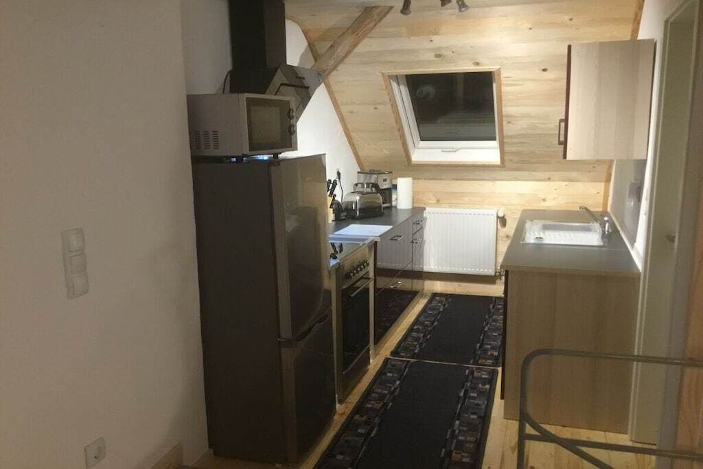 A compact kitchen with a refrigerator, microwave, and oven. There is a window above the sink and a skylight in the ceiling.